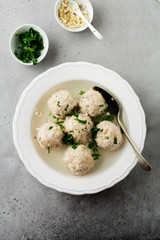 Homemade chicken matzo ball soup with parsley and garlic in simple white ceramic plate on a gray stone or concrete background.  Traditional Jewish passover dish. Selective focus. Top view.