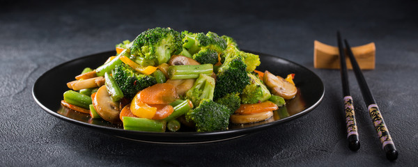 Hot stir fried vegetables on black plate. Healthy asian food concept with copy space.