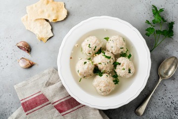 Homemade chicken matzo ball soup with parsley and garlic in simple white ceramic plate on a gray stone or concrete background.  Traditional Jewish passover dish. Selective focus. Top view.