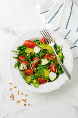 Fresh salad from arugula, tomato, avocado, olive oil, nuts and quail eggs on a light stone background. Selective focus.