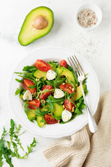 Fresh salad from arugula, tomato, avocado, olive oil, nuts and quail eggs on a light stone background. Selective focus.