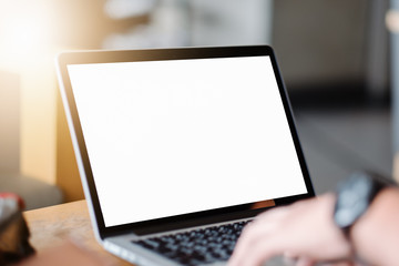 Mockup image of business man using and typing on laptop with blank white screen and coffee cup on glass table in modern loft cafe, Soft focus on vintage wooden table.