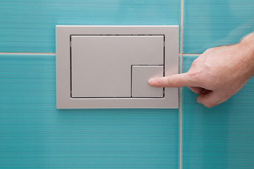 Man's hand pressing a button in the wc. Modern economic toilet flush with two separate buttons at...