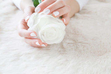 Obraz na płótnie Canvas Beautiful groomed woman's hands with white nails with artificial rose on the fluffy mat. Manicure beauty salon. Cares about clean, beautiful, soft hands skin. Healthcare concept.
