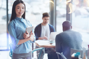 Have a break. Attractive young woman standing on the foreground and keeping smile on face while looking straight at camera