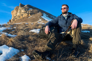 Portrait of tranquil Hipster traveler with beard in sunglasses is sitting on nature.