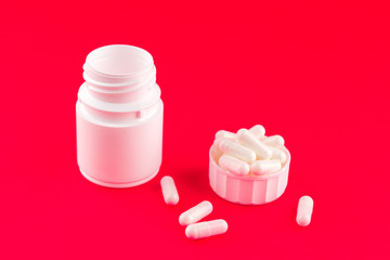 Close up white pill bottle with spilled out pills and capsules in cap on candy apple background with copy space. Focus on foreground, soft bokeh. Pharmacy drugstore concept