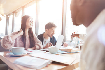 What is this. Positive delighted young woman touching her long hair while keeping smile on her face and looking at telephone of her friend