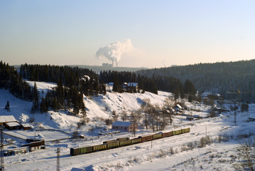 Fototapeta na wymiar view of the small railway station in the winter valley with standing freight cars; on the horizon visible smoke of industrial production..