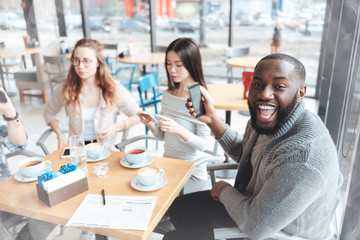 Join us. Handsome male person keeping his mouth opened while smiling and holding telephone in right hand while posing on camera
