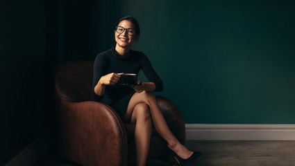 Happy female enjoying coffee while sitting on armchair