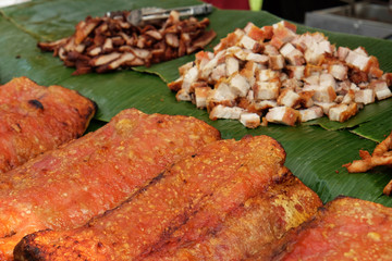 Burnt grilled crispy pork belly on banana leaf and the sliced one at the background prepared for selling in street market