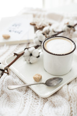 Mug of hot drink with cotton branch on white cozy winter blanket