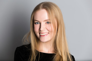 portrait of a young beautiful blond woman with evening make-up in a black shiny dress near a gray wall