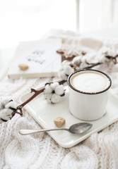 Mug of hot drink with cotton branch on white cozy winter blanket