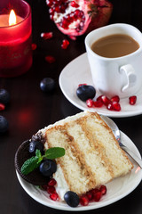 Piece of layer cake with fresh blueberries, cream cheese and chocolate cookies. Dark wooden background. Pomegranate and burning candle. Romantic Valentine's Day concept. Selective focus.