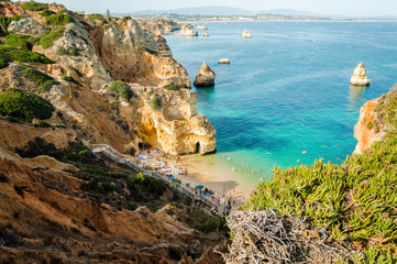 Fototapeta na wymiar Camilo Beach in Lagos, Algarve, Portugal. A tiny secret beach between the limestone walls. 200 wooden steps down to sheltered, sandy cove divided by ochre-colored rocks with hand-dug tunnel.