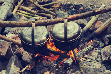 Two pots, covered with soot, are hanging over a campfire