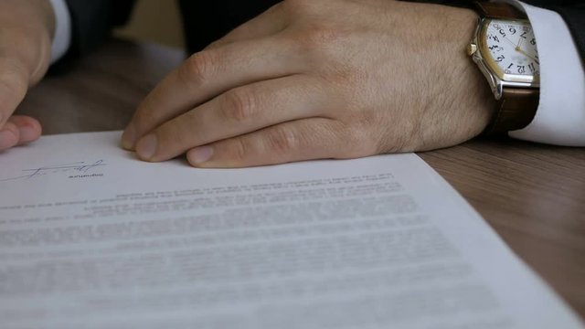  The man corrects and fills the document. Businessman signing business contract agreement, close up of male hand with pen writing signature.