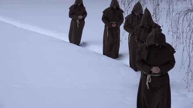 Group of monks in hood robe walking along winter snow trail