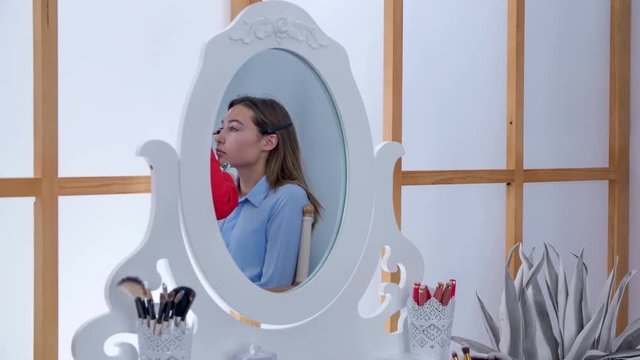 We can see a relection of the client's face in the mirrow. A make up artist is doing her make up.