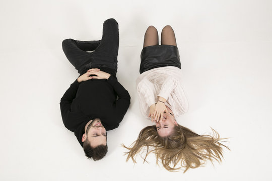 Young Loving Couple, Young Man And Girl With Long  Hair Having Fun Talking To Each Other, Lying On Back On  Floor On White Background