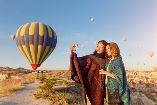 Couple of friends travelers enjoying valley view and making selfie on a phone with wonderful balloons flight over Cappadocia valley in Turkey