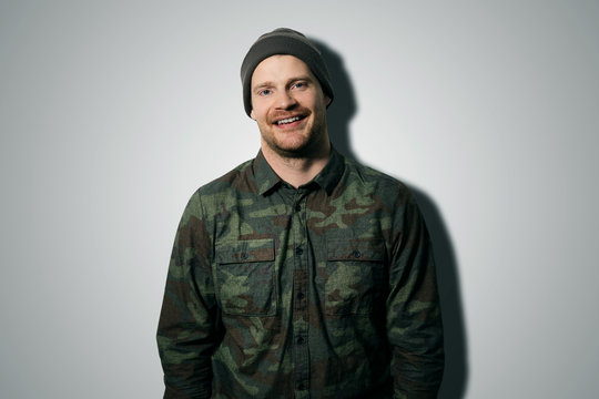 young attractive man wearing camouflage long sleeve shirt and hat on gray background