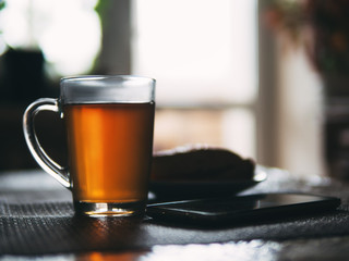 winter morning . mug of hot black tea and cake with the phone on the table the light from the window