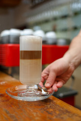 Hand barista holding and serving glass of latte.