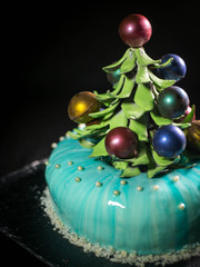 Contemporary Cake covered with blue chocolate mirror glaze and decorated with chocolate elements of Christmas tree, on dark background.