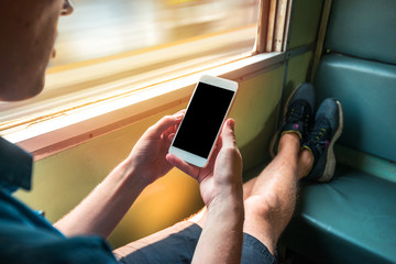 Man sitting in a train in motion holding a phone in his hands. Light by the window