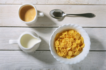 Corn Flakes cereal in a bowl, glass with milk and cap with espresso coffee. Morning breakfast.