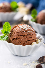 Chocolate ice cream scoop in white bowl with chopped white chocolate and mint decoration. Summer food concept with copy space.
