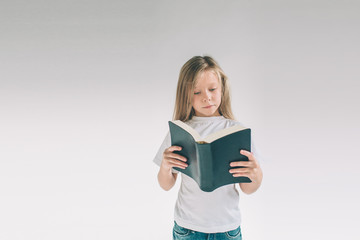 girl in white t-shirt is reading a book on a white background. Child likes to read books