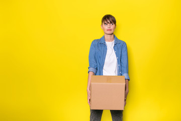isolated woman on yellow with cardboard box - obrazy, fototapety, plakaty