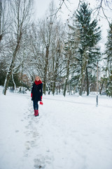 Blonde girl in red scarf and coat walking at park on winter day.