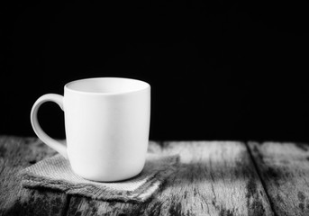 A white mug on the wooden table on dark background, Black and white filter