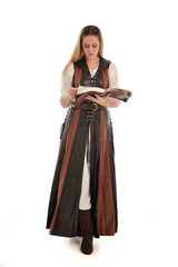 Fototapeta premium full length portrait of girl wearing brown fantasy costume, holding a book. standing pose on white studio background. 