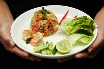 Fried rice with shrimp topped sliced red hot chili pepper,sliced cucumber ,halved green lemon and garlic on white plate.