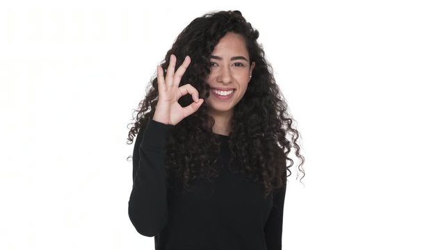 Portrait of charming curly long haired adult girl happily showing thumb up isolated on white background. Concept of emotions