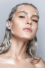 Beautiful woman portrait with pearl beads on face, silver hair and wet skin and sinver hands.