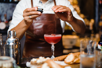 Barman in a brown leather apron making fruit alcoholic cocktail