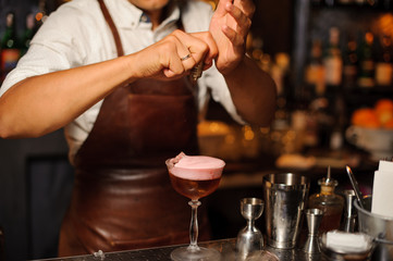 Fototapeta na wymiar Barman in a brown leather apron making fruit alcoholic cocktail with foam