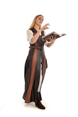  full length portrait of girl wearing brown  fantasy costume, holding a book. standing pose on white studio background. 