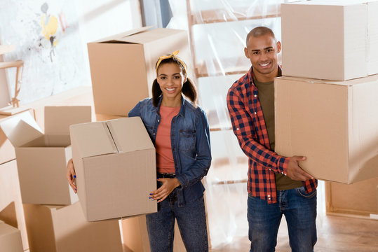 beautiful african american couple holding cardboard boxes and moving to new home