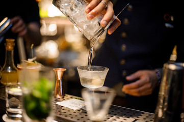 Barman pouring alcoholic drink into the glass on the bar counter