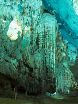 Adult woman with a backpack stands in beautiful cave with stalactites and stalagmites in Phong Nha Cave in Phong Nha-Ke Bang National Park, QUANG BINH, VIETNAM