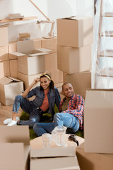 african american couple resting on floor in new home with cardboard boxes
