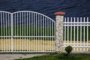 Minimalist seaside yard/White fence with stone masonry enclosing a yard with a view of the sea.